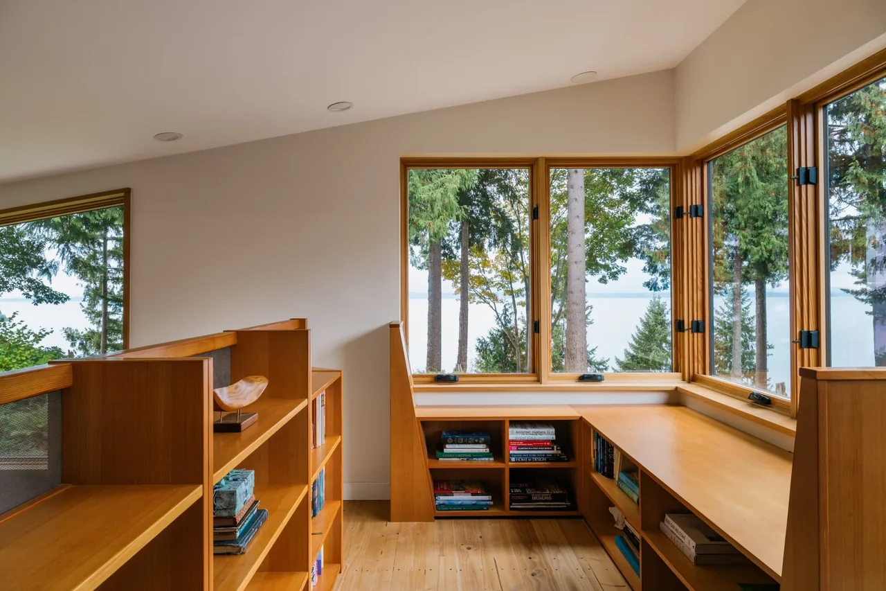 Office nook features built-in wood bookshelves and corner windows with forest and ocean views in Edmonds Overlook project.