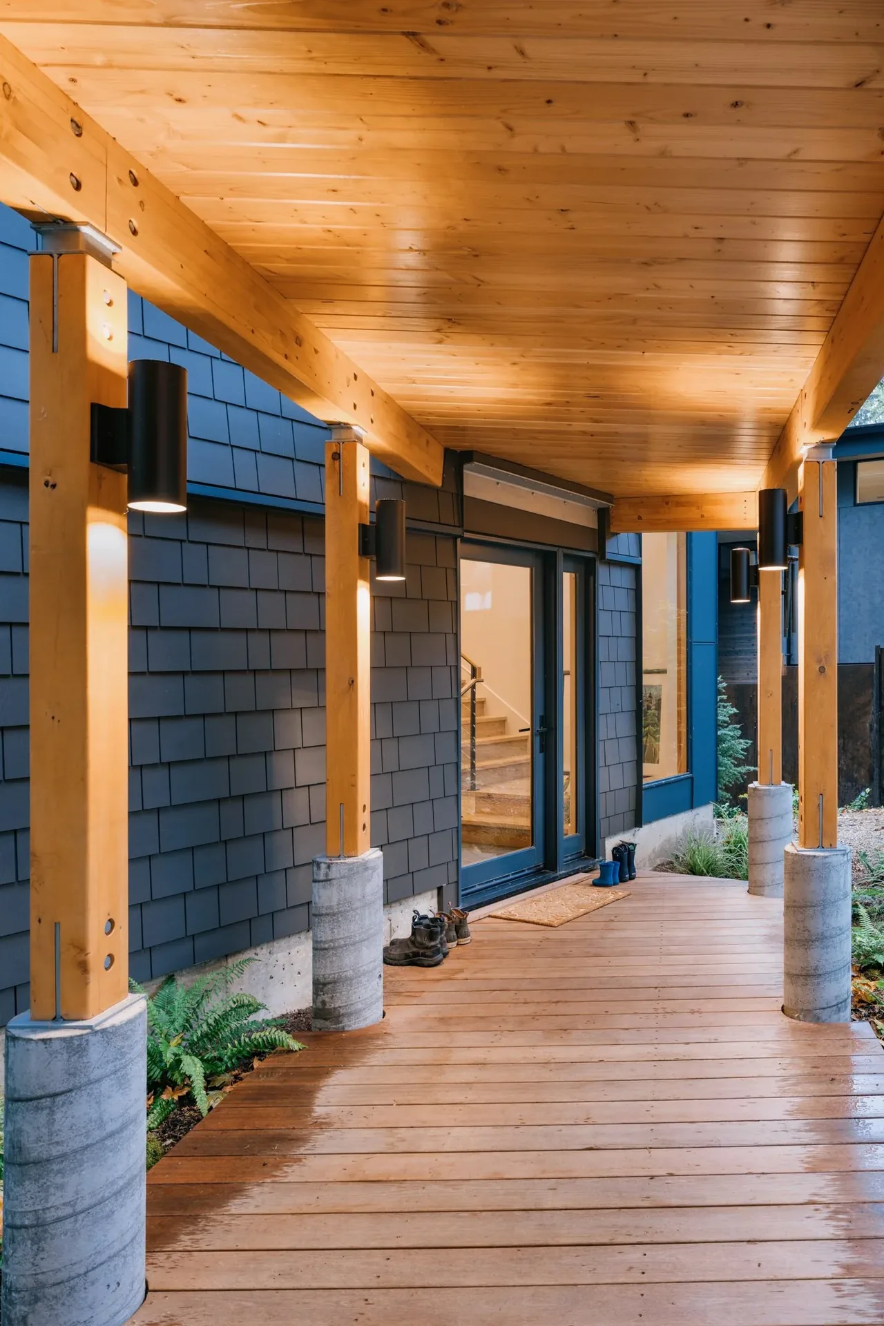 Covered patio with wooden deck and black shingle siding on the house exterior.