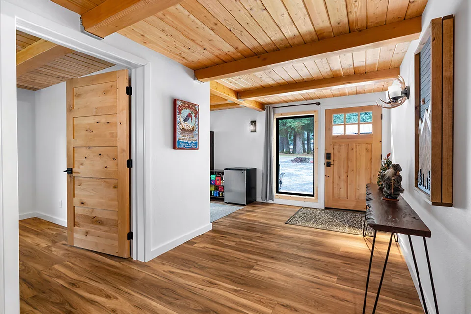 Entry with natural wood ceiling and floors, a wooden front door, and a black-framed window beside it.