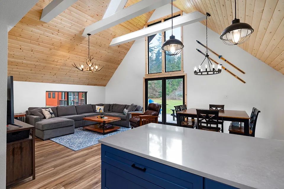 Vaulted ceiling living and dining space with wood paneling, modern lighting, and large glass doors opening to a yard.