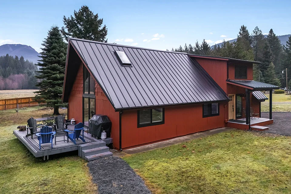 Exterior view of a remodeled red house with a gable roof, black window frames, and an outdoor deck with seating.