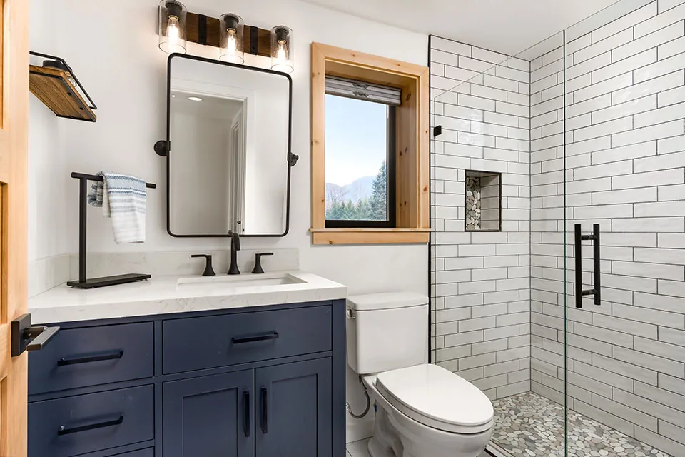 Bathroom featuring a navy blue vanity with white quartz countertop and modern tiled shower with pebble floor and black fixtures.