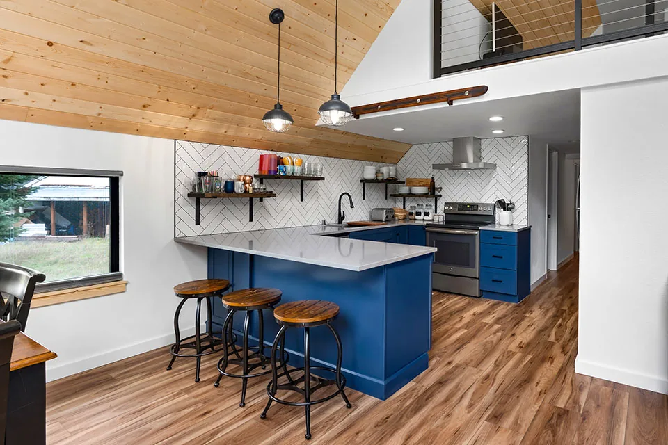 Kitchen features blue cabinets, wood ceilings, and a white tile backsplash in a herringbone pattern.