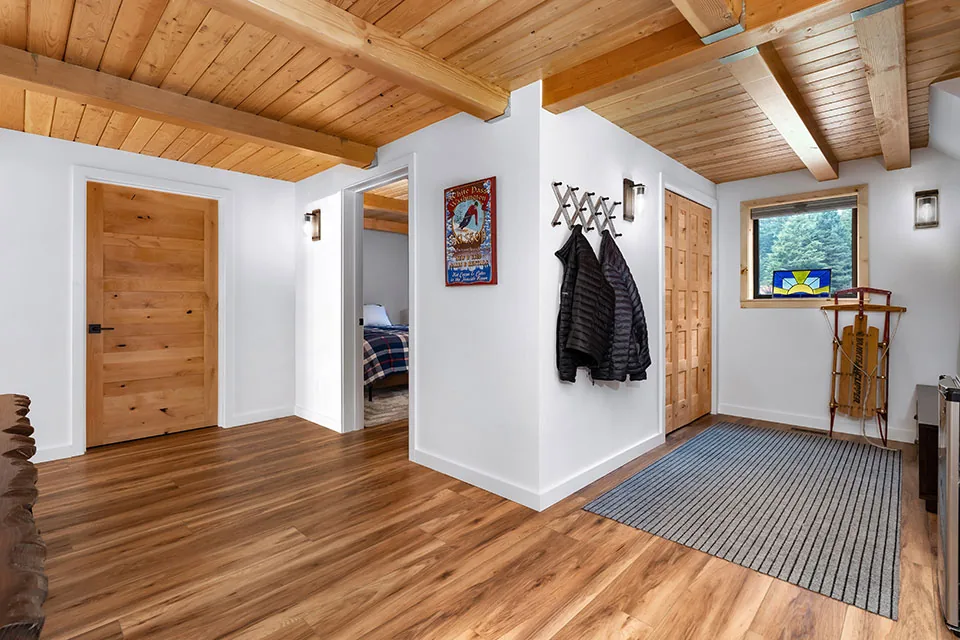 The Crescent Beach Remodel Draft features a hallway with wood-clad ceiling, multiple wood doors, and an area rug near the window.