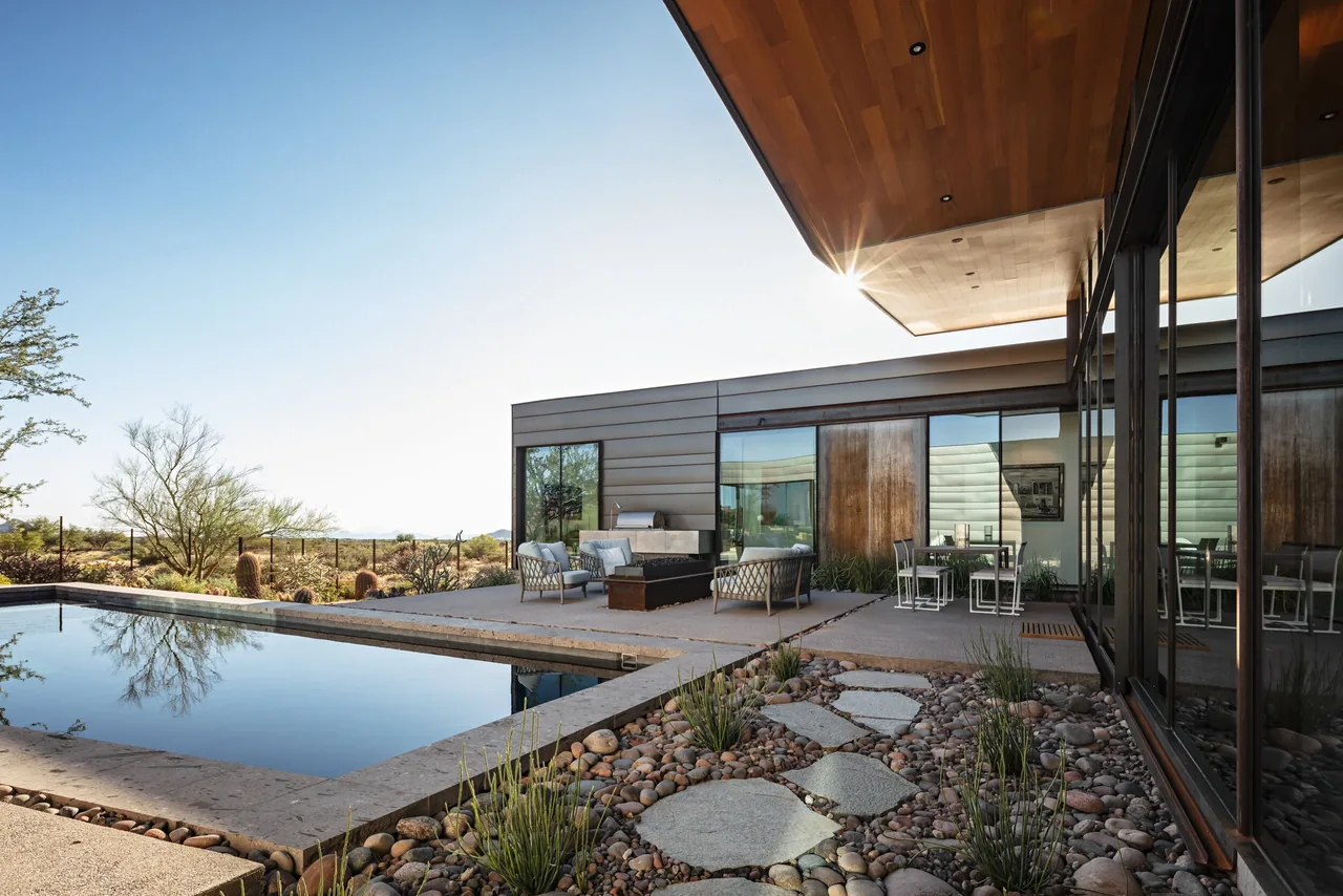 Outdoor living space features a reflective pool, seating area with contemporary furniture, and desert landscaping beyond.