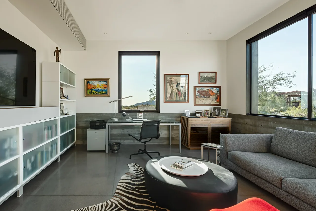 A modern home office with floating desk, leather ottoman, and large windows overlooking desert scenery.