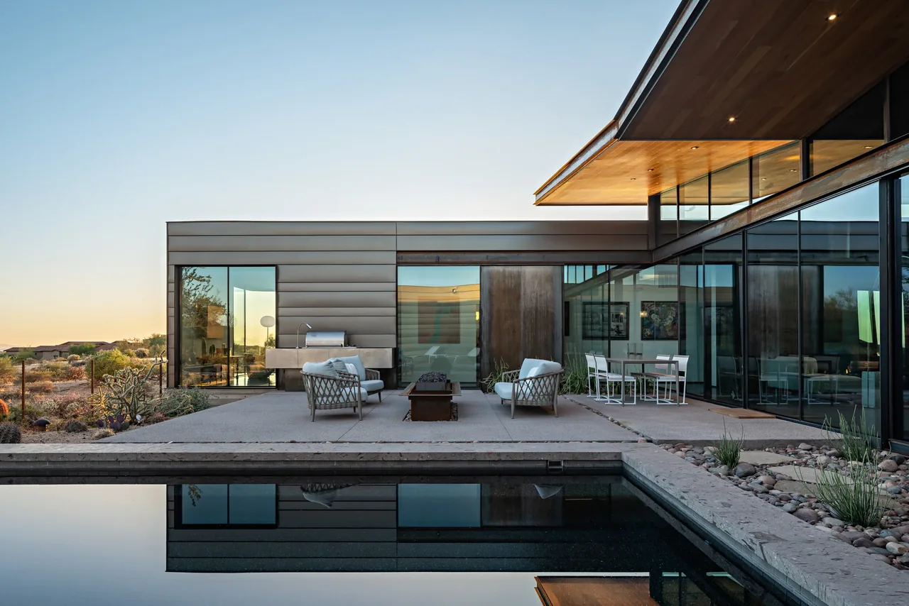 Exterior rear patio of a modern single-story home featuring outdoor seating and large glass walls overlooking a pool.