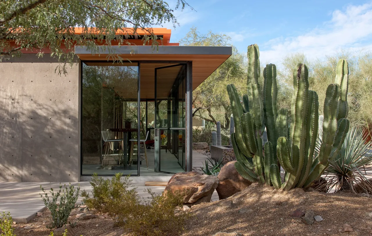 The barn guest house features floor-to-ceiling black-framed glass walls and a flat roof with exposed wood soffit.