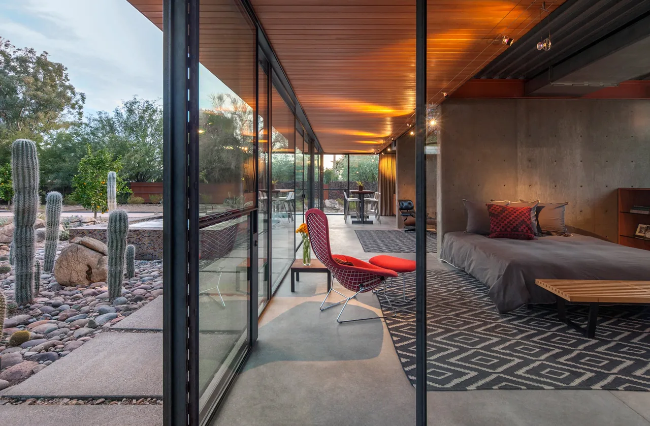 Barn guest house bedroom with concrete walls, glass sliding doors, and desert landscaping visible outside in Phoenix.