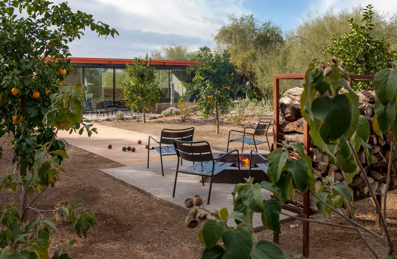 The barn guest house features an outdoor seating area with a fire pit surrounded by metal chairs amid desert landscaping and citrus trees.