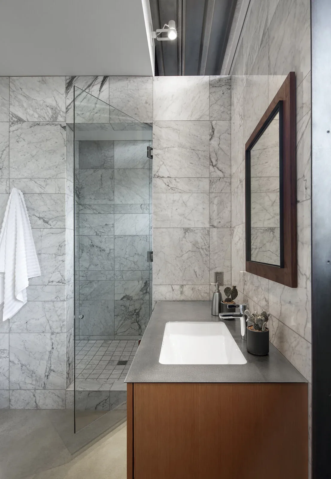 Bathroom features marble tile walls, a concrete countertop with built-in sink, and a frameless glass shower door.