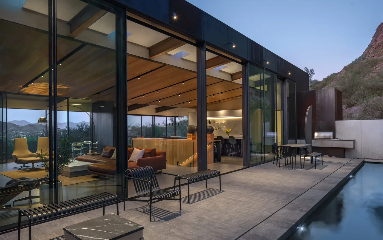 The cliffback project features floor-to-ceiling glazing opening to a patio with pool, integrated into the desert rock landscape.