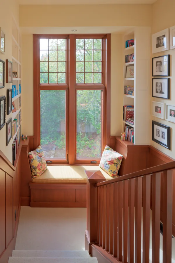 Stair landing features a built-in wooden window seat with floral cushions and large divided lite windows.