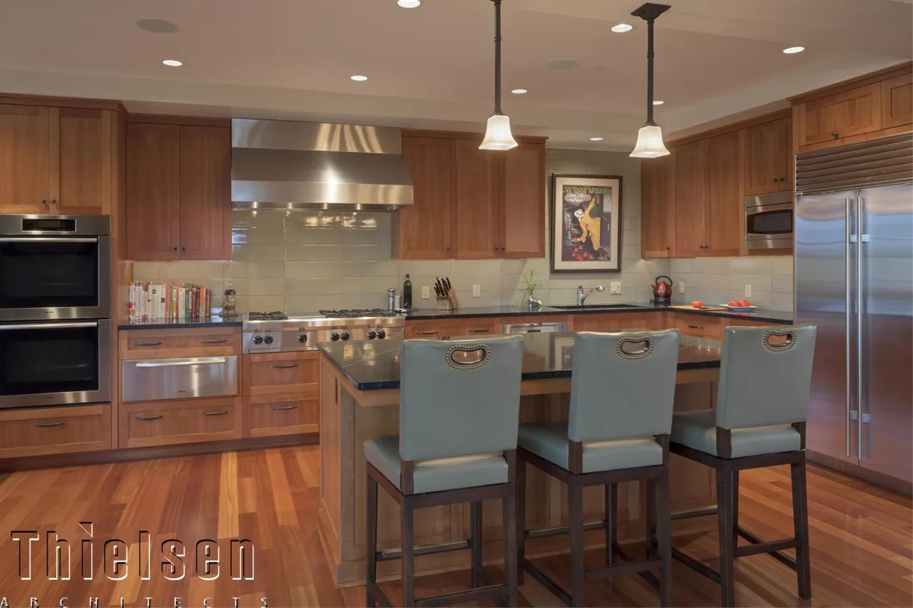 The Roanoke Residence kitchen features wood cabinets, a large island with seating, and stainless steel double ovens and refrigerator.