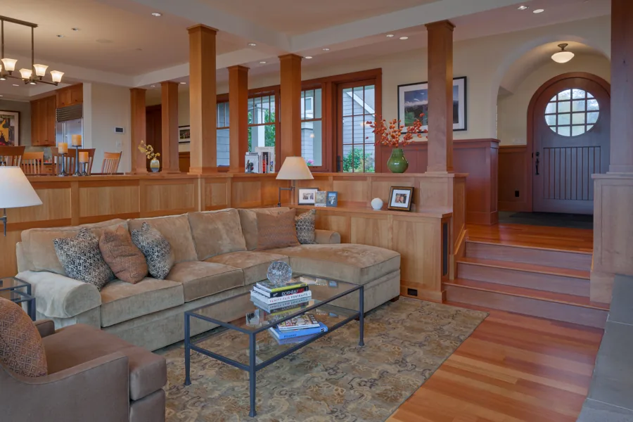 The living area in the Roanoke Residence features wooden paneling and a beige sectional sofa facing a glass coffee table.