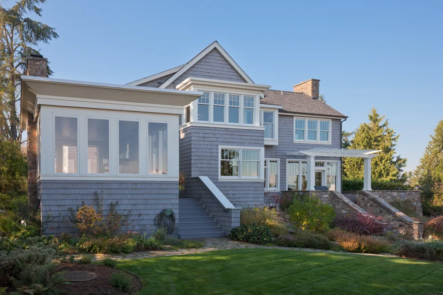 Rear exterior of a two-story house with shingle siding, multiple windows, and a covered patio with stone stairs surrounded by landscapedgard