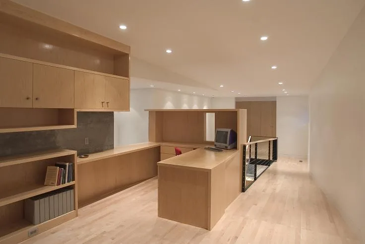 Office space with light wood built-in cabinets and desk adjacent to a stairwell with wood railing and metal balusters.