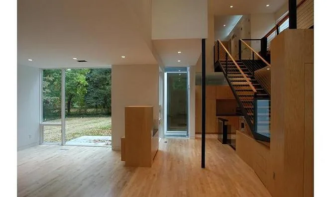 Open living space with floor-to-ceiling glazing and a floating staircase in light wood and black metal.