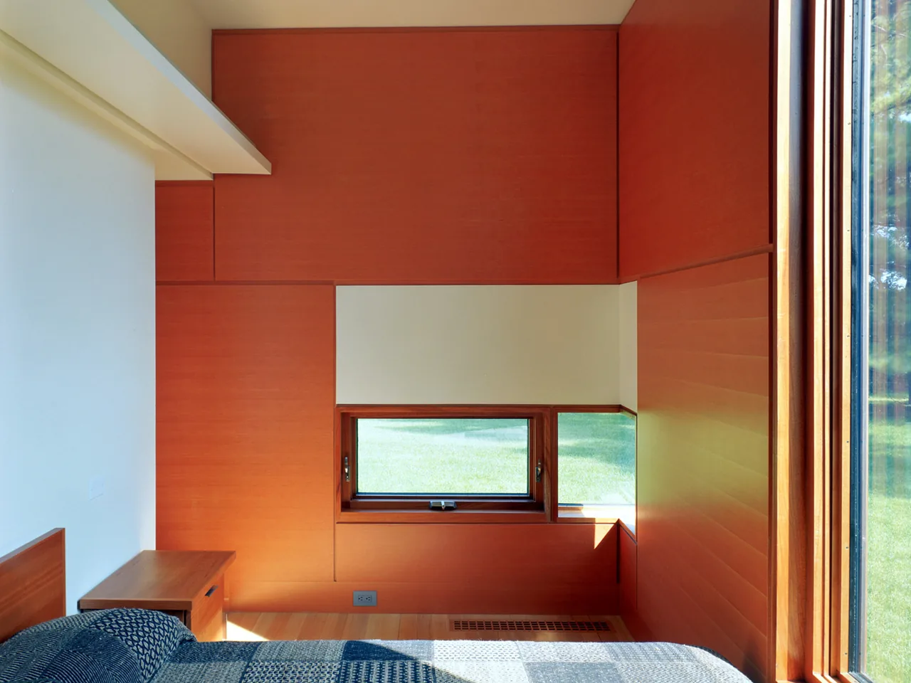 Red wood-paneled bedroom with a small horizontal window and floor-to-ceiling glass door to the outdoors.