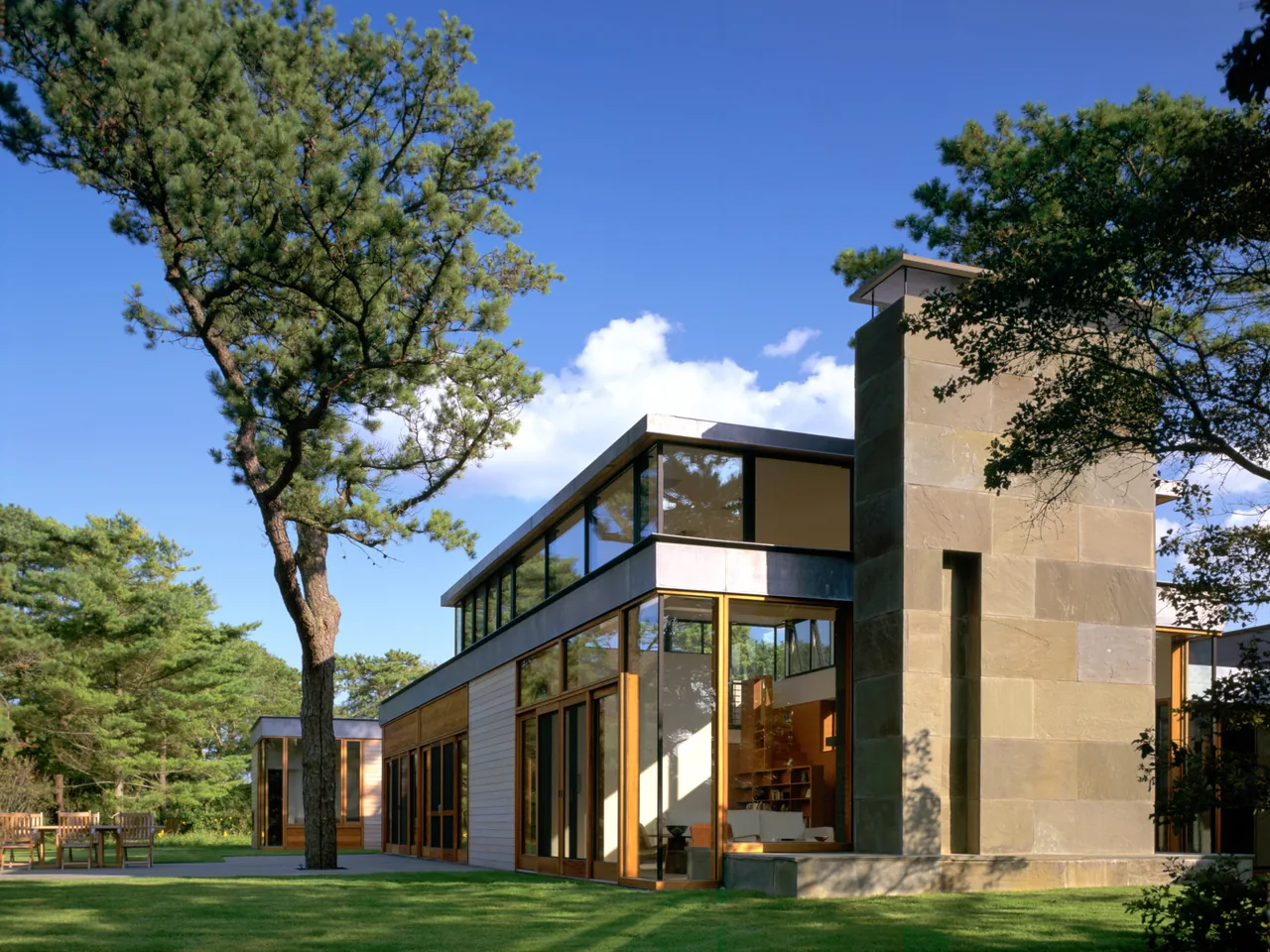 Exterior view of Long Island House featuring large glass panels and a prominent stone chimney.