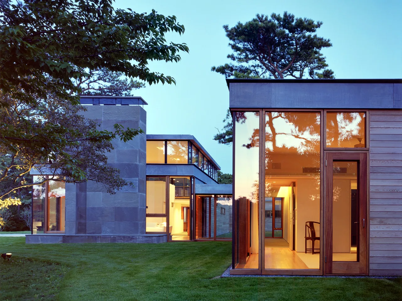 Long Island House by Tod Williams Billie Tsien Architects features large floor-to-ceiling glass windows and a combination of stone and wood siding.
