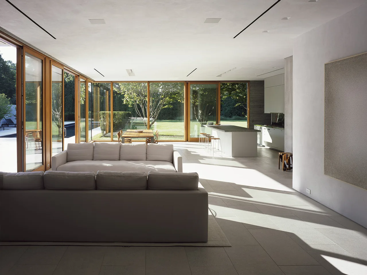 Open living and kitchen area with floor-to-ceiling wooden framed glass walls at Further Lane House.