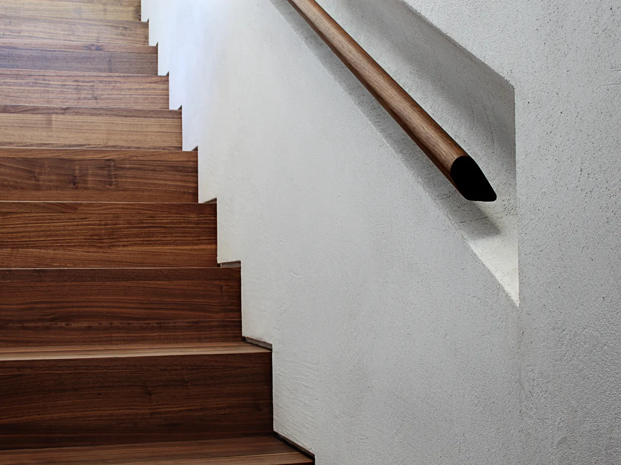 Wooden stairs with a matching handrail built into a white plaster wall.