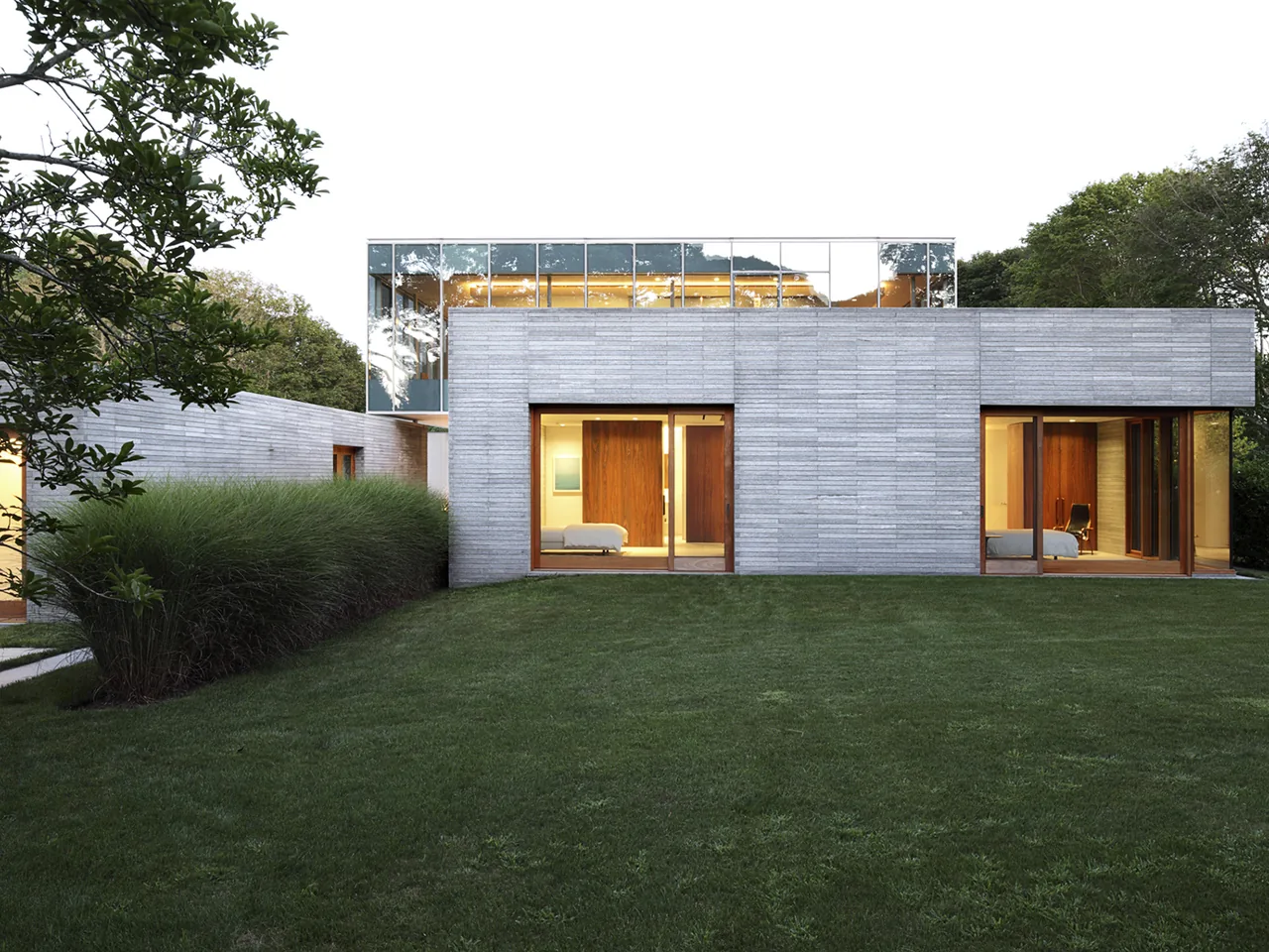 Further Lane House features textured concrete walls and large windows overlooking the green backyard in New York.