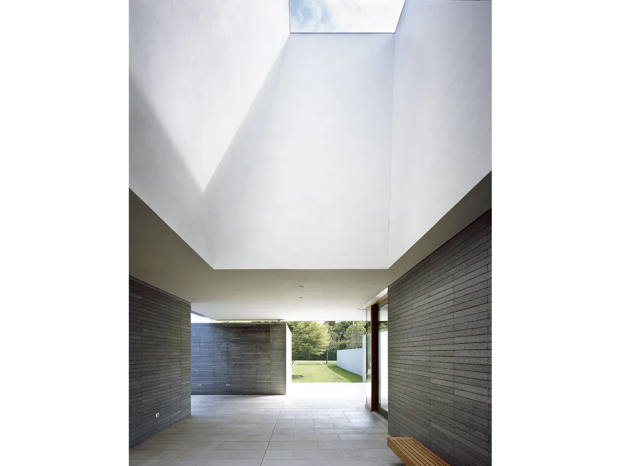 Covered outdoor space in Further Lane House with dark brick walls and a large square skylight opening to the sky.