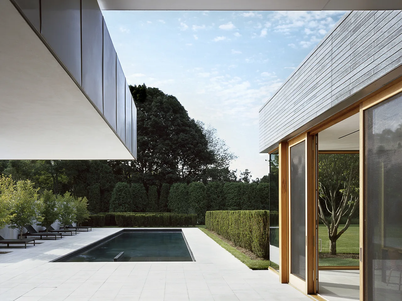 The Further Lane House features a minimalist outdoor pool area with clean lines and glass doors opening to the garden.