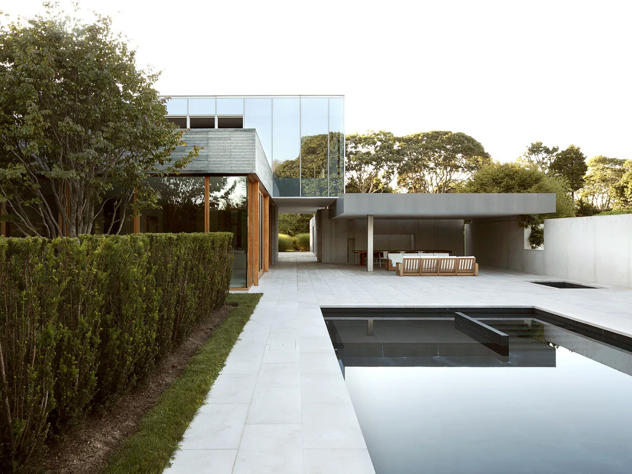 Further Lane House features a minimalist pool deck with a black pool liner and a covered patio with seating.