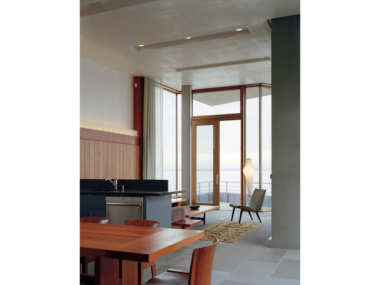 Shelter Island House kitchen and living area showing wood table, built-in bench, and glass doors to balcony.