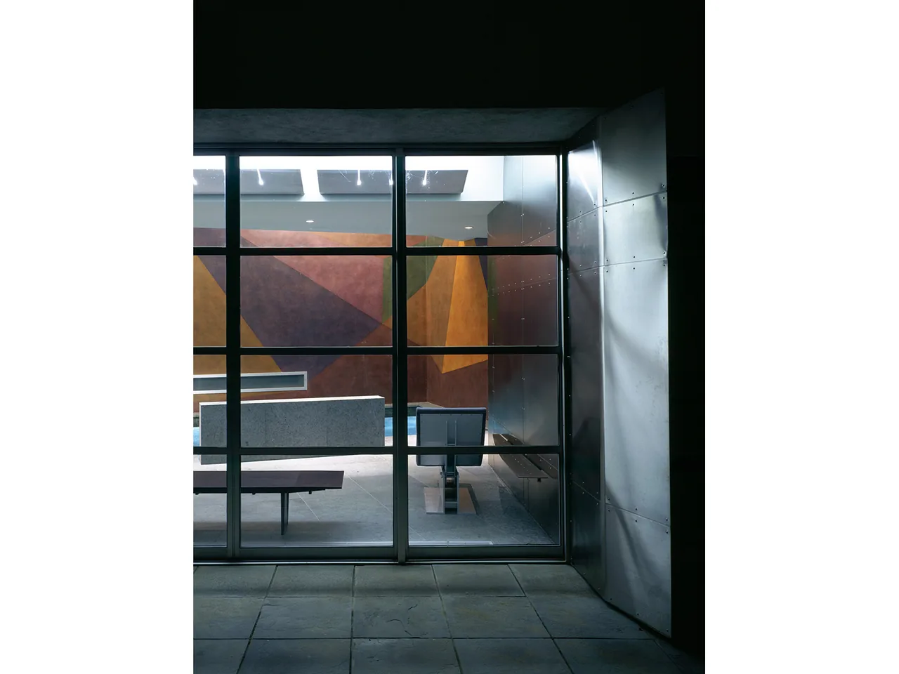 Pool House features a geometric mural wall and modern seating visible through a large metal grid window.