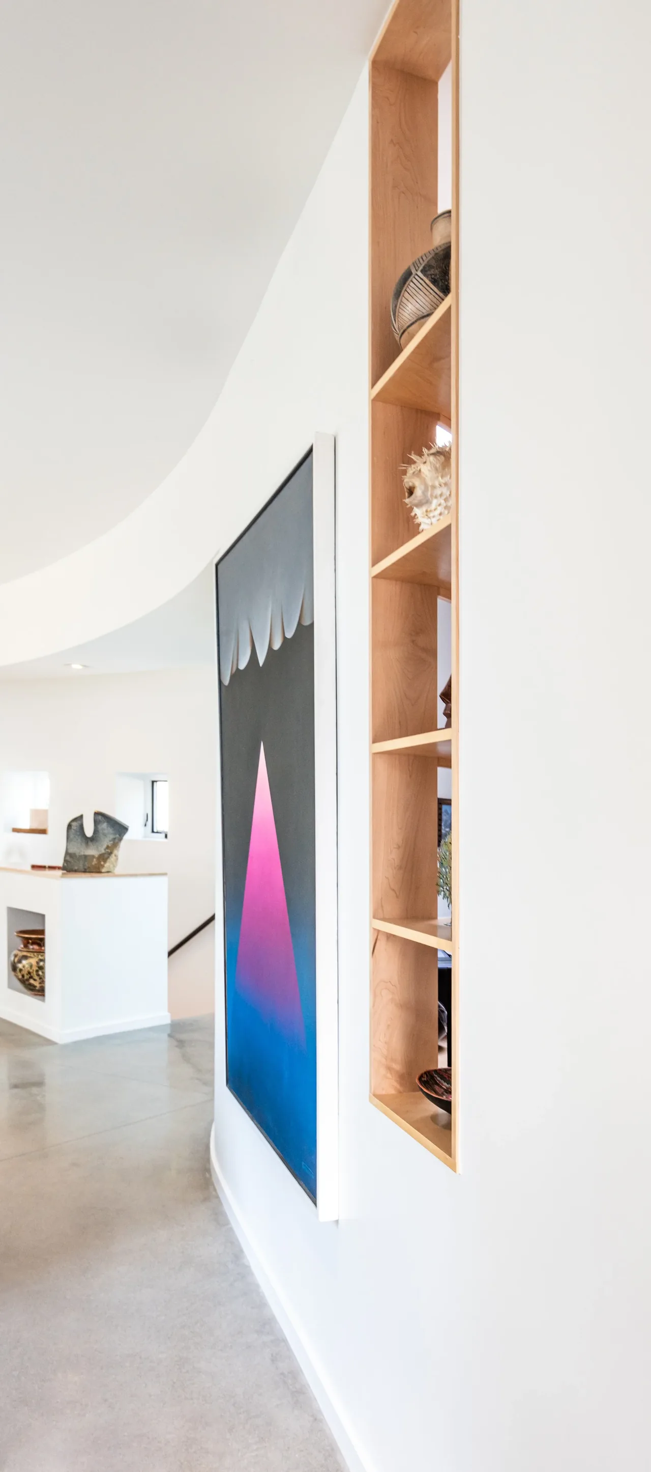 Curved hallway wall features an abstract art piece and recessed wood shelving with decorative items in the Jefferson St. Residence.