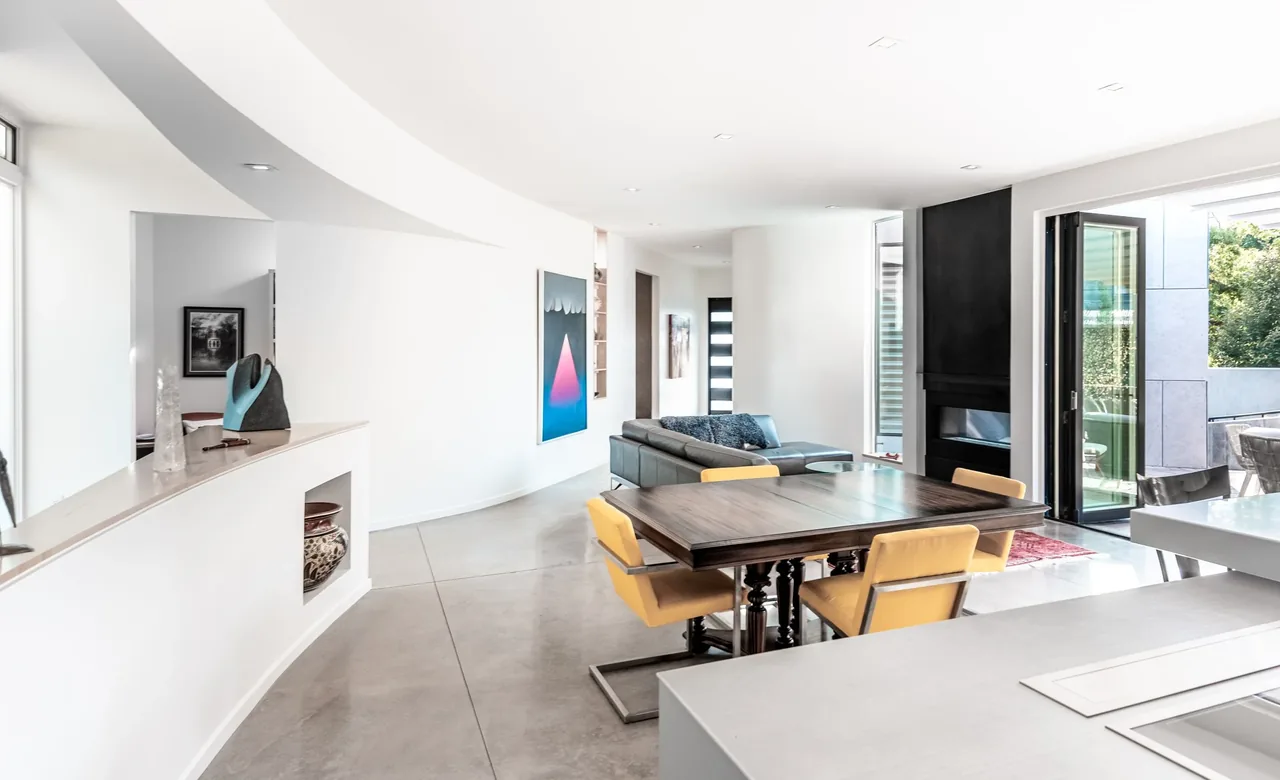 Dining and living space with curved ceiling and walls, polished concrete floors, and sliding glass doors opening to an outdoor area.