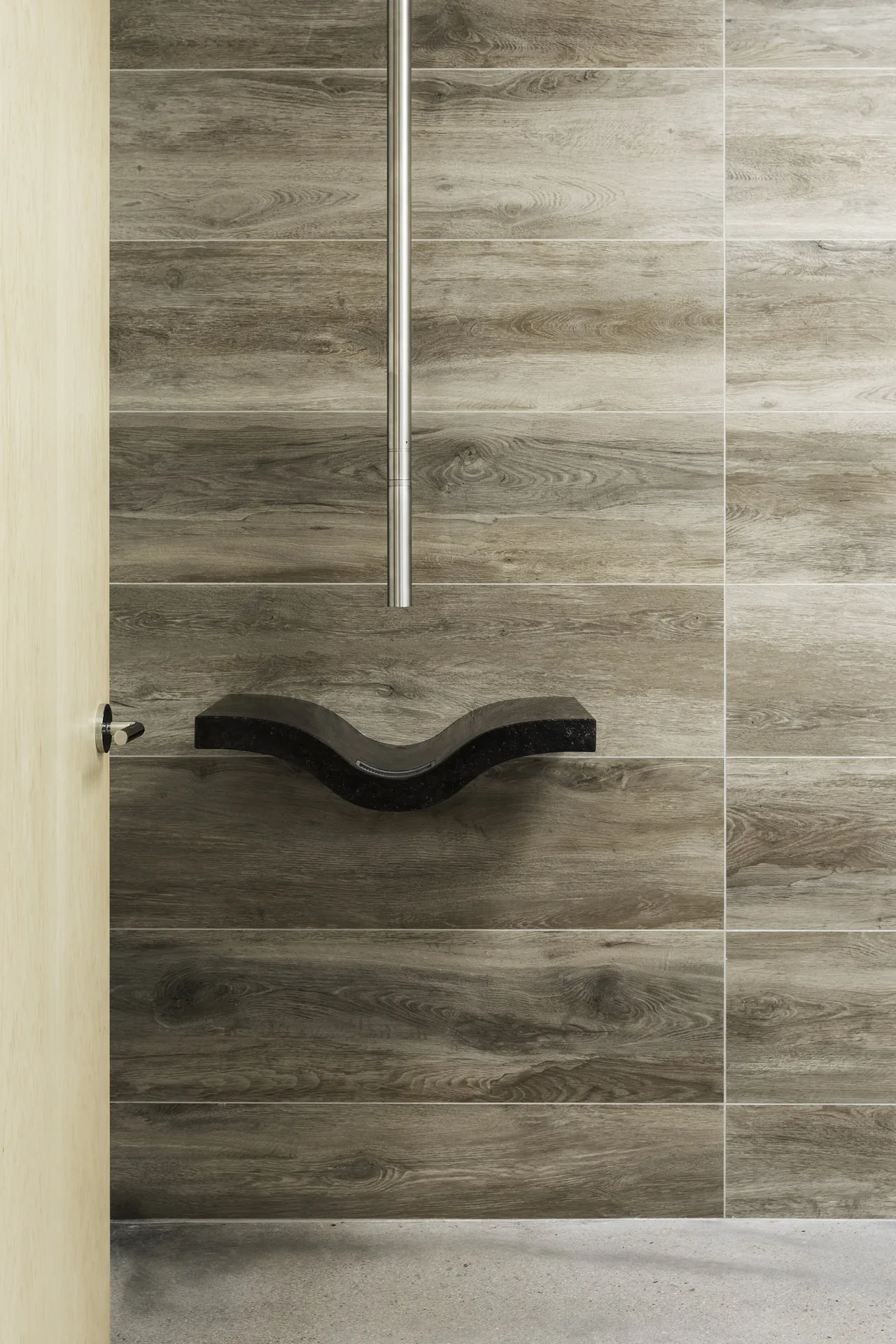 Modern bathroom with curved black vessel sink mounted on wood-look tile wall and thin vertical faucet.