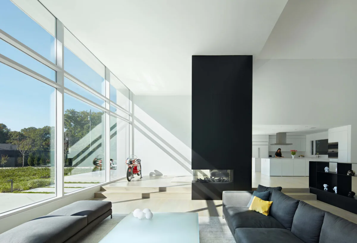 Living room with floor-to-ceiling glazing and a black modern fireplace separating the seating area from the kitchen.