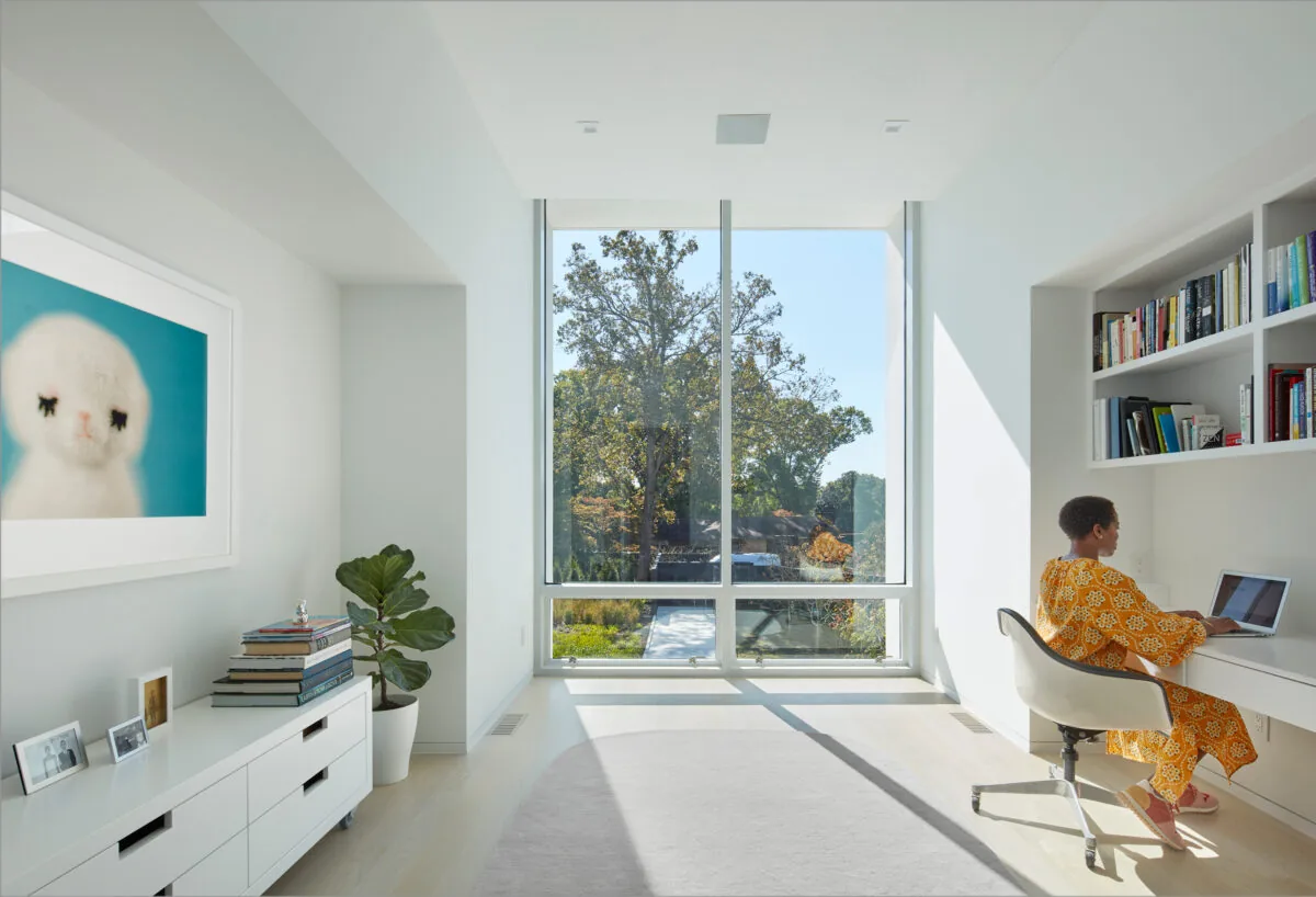 Bright home office with floor-to-ceiling glazing and built-in shelving, designed for natural light and workspace functionality.