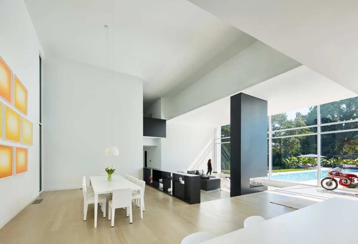 Frame House living and dining area with floor-to-ceiling glazing and a black fireplace column by Tonic Design & Construction.