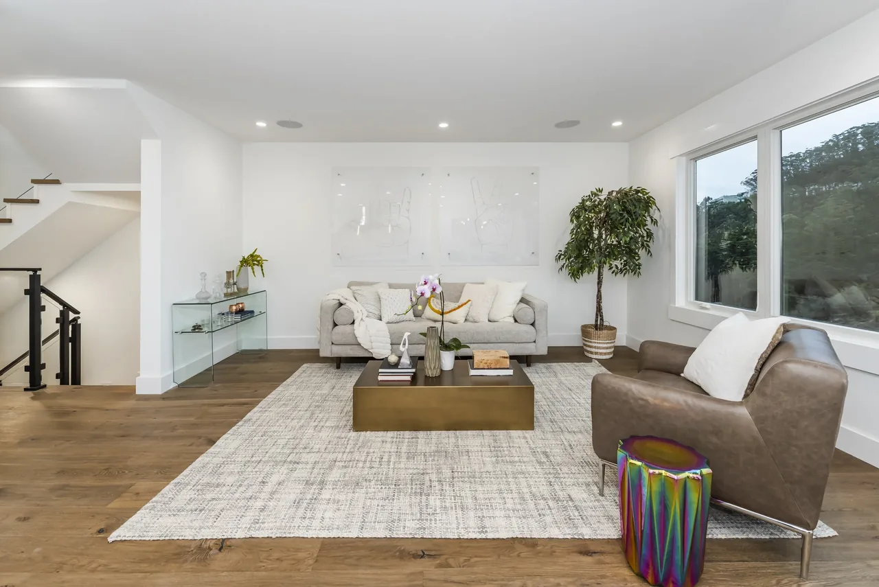 Living room with contemporary furniture, a large area rug, and wide windows overlooking greenery.
