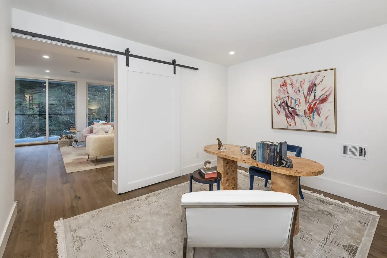 Home office space with wooden desk and sliding barn door leading to living area overlooking wooded view.