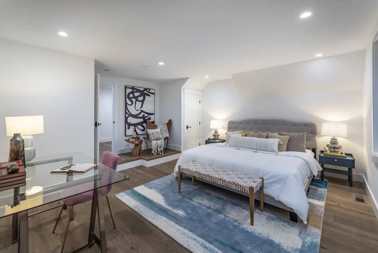 Bright bedroom with a gray tufted headboard, area rug, and seating nook featuring abstract art.