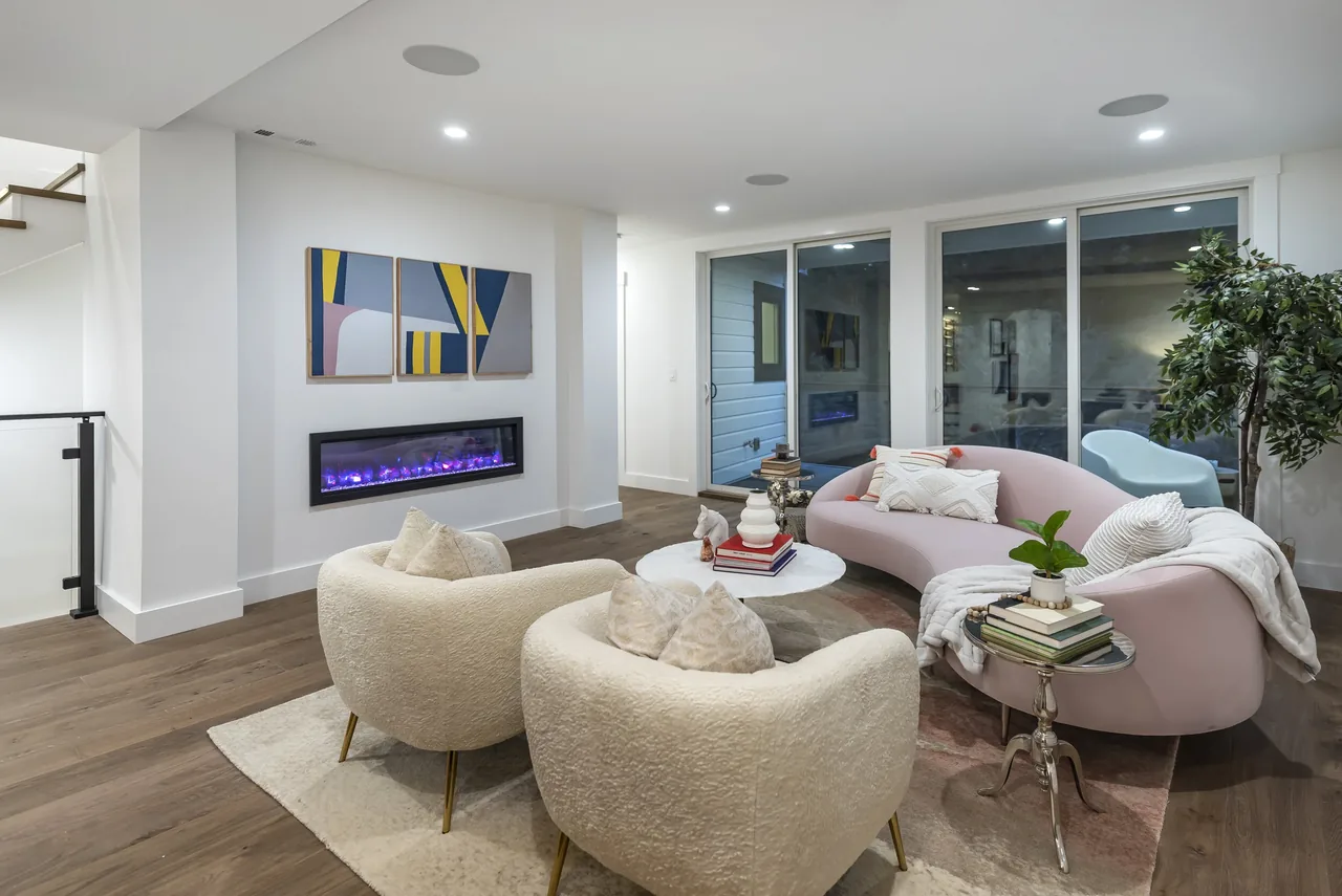 Forrest Edge living room features a curved pink sofa, electric fireplace, abstract triptych art, and sliding glass doors leading outside.