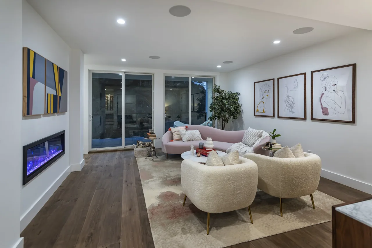 Living room features a curved sofa, abstract paintings, and a built-in linear fireplace with glass sliding doors.