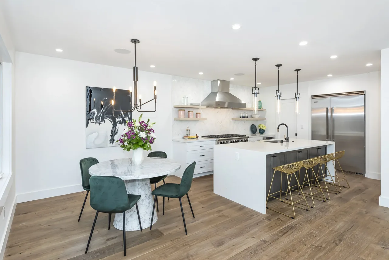 The Forrest Edge kitchen features a round marble dining table, gold metal bar stools at the island, and stainless steel appliances in a bright open layout.