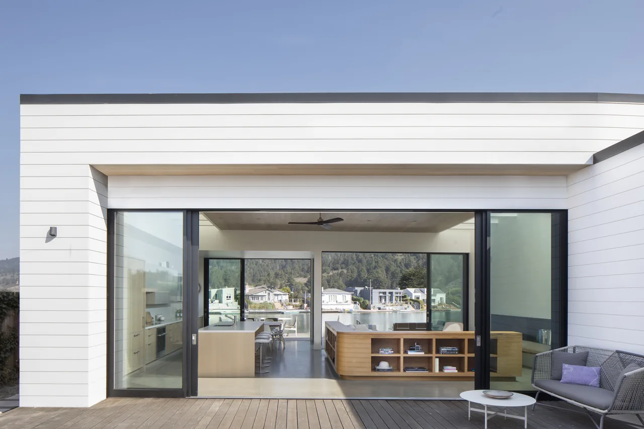 Dune House exterior features white horizontal siding and floor-to-ceiling glazing with black frames opening to the interior.