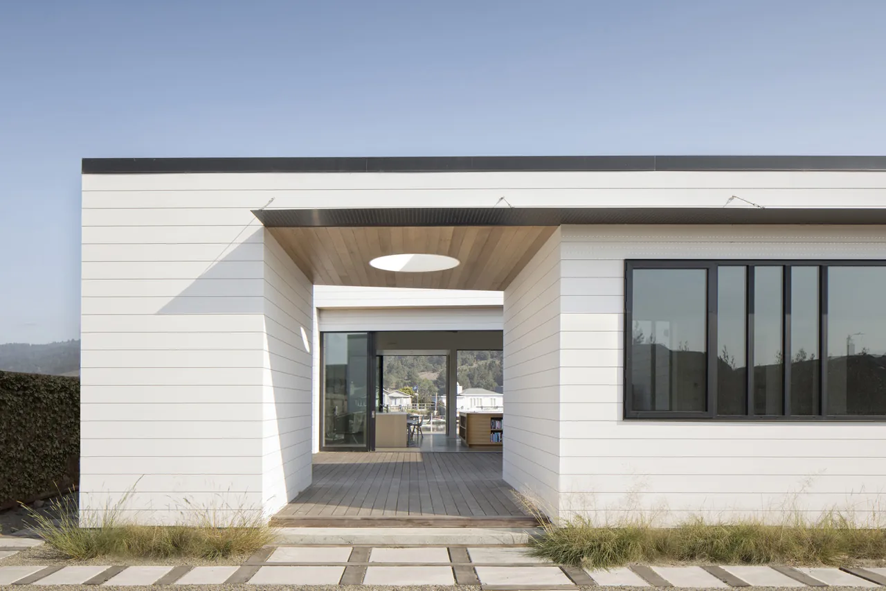 Dune House exterior with white horizontal siding, covered entry with circular skylight, and black-framed windows.