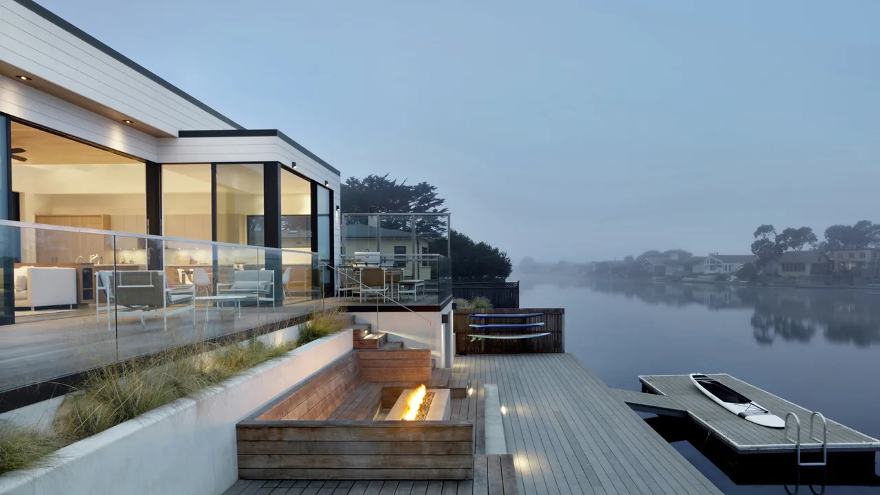 Dune House features floor-to-ceiling glazing and a waterfront dock with a built-in wooden fire pit seating area.