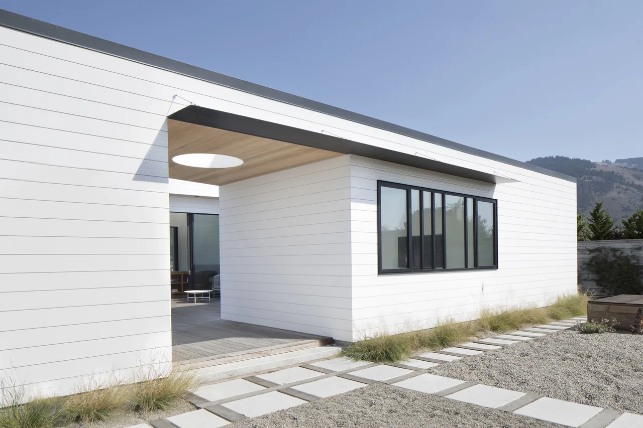 The Dune House features modern white horizontal siding and a covered patio with a circular skylight opening.