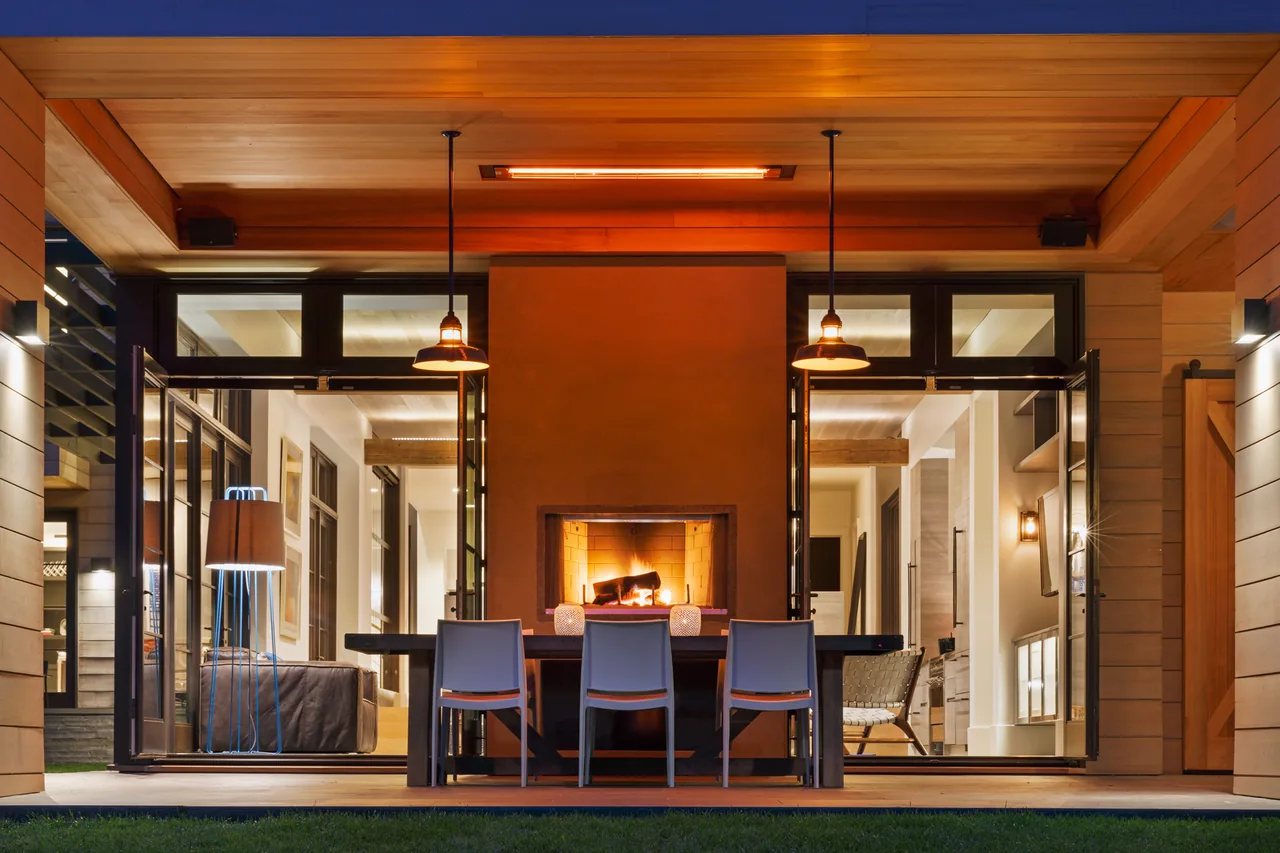 The Watermill Residence features a covered patio dining space with a central outdoor fireplace and pendant lighting.